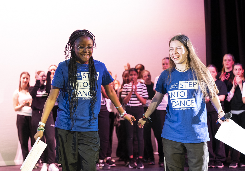 Two students who have hosted an event about to take a bow. Students seen behind them applauding.